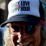 Trucker hat with black mesh back and white front panel with Peace Love & Happy Hour logo in black and red on front.